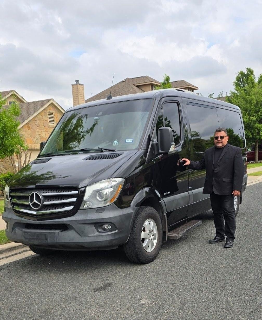 An Ubiquitous Driver chauffeur in a suit beside a Sprinter van